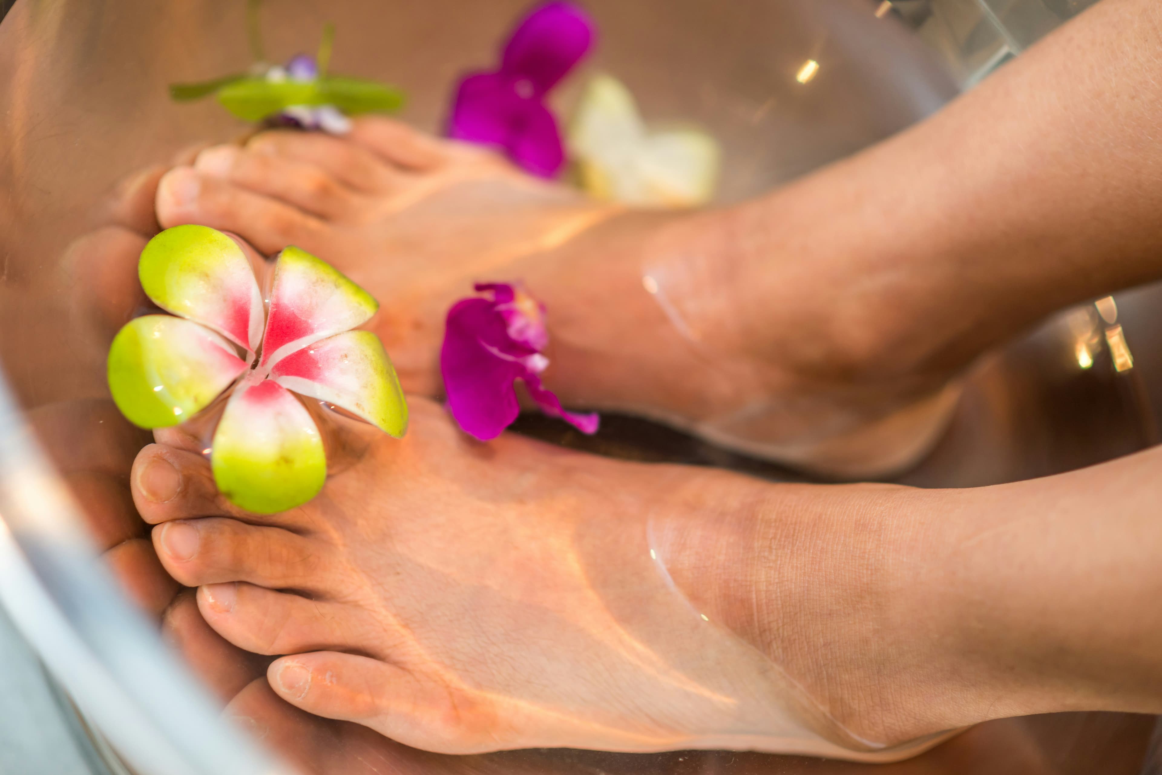 Feet in a warm pedicure bath scattered with flowers