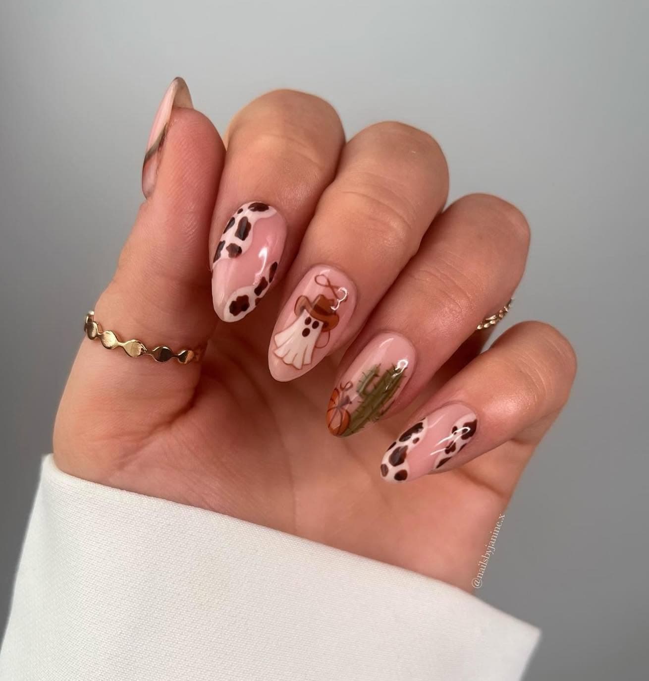 Nude almond nails with hand-painted cow print, cactus and cowboy ghost designs